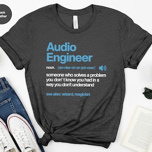 May include: Black heather t-shirt with the text "Audio Engineer" in blue. The shirt includes a definition of the term, along with the phonetic pronunciation. The shirt is paired with blue jeans and white sneakers.