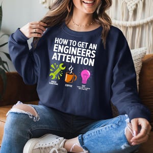 Navy sweatshirt with "How to Get an Engineer's Attention" and three icons.
