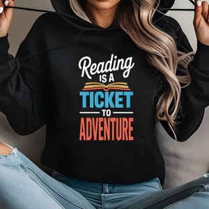 Black hoodie with "Reading is a ticket to adventure" and an open book graphic.