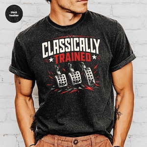 May include: Black heather t-shirt with the text "CLASSICALLY TRAINED" in white and red, featuring a graphic of three car pedals. The design includes red star accents and a distressed look.