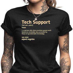May include: Black t-shirt with the text "Tech Support" in gold lettering. The definition of "Tech Support" is printed below, describing the role as a person who does precision guess-work based on unreliable data. The shirt also lists "wizard, magician" as related terms.