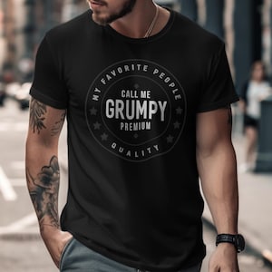 May include: Black t-shirt with a circular graphic that reads "My Favorite People Call Me Grumpy Premium Quality." The design is in white and gray. The shirt is short-sleeved and appears to be made of a soft material.