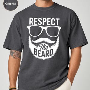 May include: Graphite-colored t-shirt with a white graphic of a beard, mustache, and glasses, with the words "RESPECT The BEARD". The shirt has short sleeves and a crew neck.
