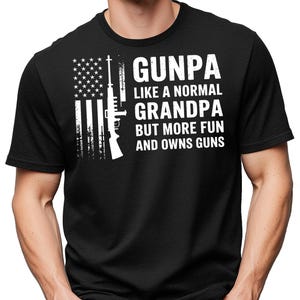 May include: Black t-shirt with a white graphic featuring an American flag design and a rifle silhouette. The text reads "GUNPA LIKE A NORMAL GRANDPA BUT MORE FUN AND OWNS GUNS."