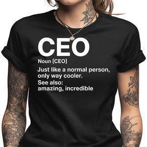 May include: Black t-shirt with the word "CEO" in large white letters. Below the word "CEO" is the definition of CEO, followed by the phrase "Just like a normal person, only way cooler." The shirt also says "See also: amazing, incredible."