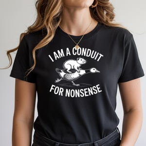 May include: Black t-shirt with a humorous graphic. The design features a white rodent riding a goose, with the text "I AM A CONDUIT FOR NONSENSE" in white. The shirt is a casual wear item.