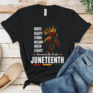 May include: A black t-shirt featuring a graphic of a person wearing a crown and headwrap, with the text ROOTS, BEAUTY, STRONG, MELANIN, QUEEN, LEGACY, Remembering My Ancestors, and JUNETEENTH, accented by red, yellow, and green horizontal brush strokes.