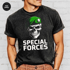 May include: Black heather t-shirt featuring a skull wearing a green beret with a white button. The skull graphic is above the words "SPECIAL FORCES" in bold white letters. The shirt has rolled-up sleeves.