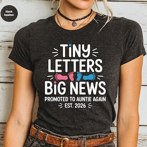 May include: Dark gray t-shirt with the text "TINY LETTERS BIG NEWS" in white. Pink and blue footprints are below the text. The shirt also says "PROMOTED TO AUNTIE AGAIN EST. 2026".