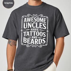 May include: Graphite-colored t-shirt with the text "AWESOME UNCLES HAVE TATTOOS AND BEARDS" in a white decorative frame. The shirt has short sleeves and a relaxed fit, suitable for casual wear.
