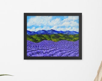 Op de afbeelding: Een ingelijst schilderij van een lavendelveld met glooiende heuvels op de achtergrond. De lucht is blauw met witte wolken. Het schilderij is in een zwarte lijst.
