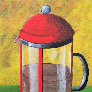 May include: A red and clear glass French press coffee maker with a black handle. The coffee maker is filled with dark brown coffee and is sitting on a green surface.