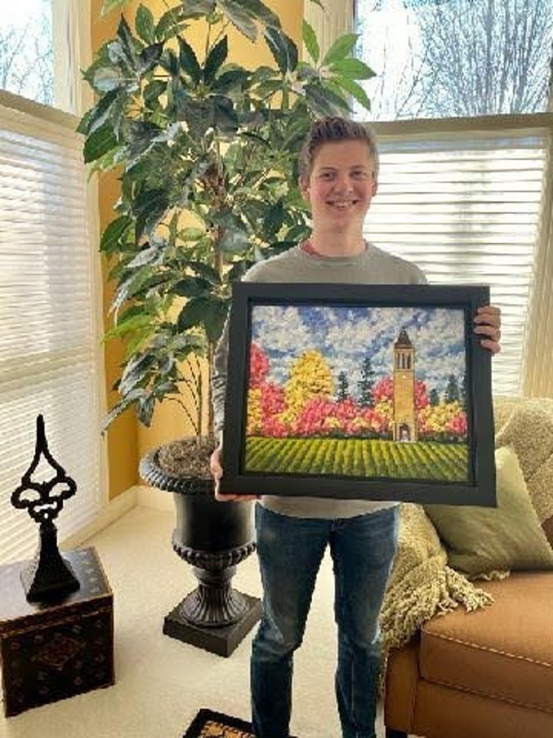 May include: A framed landscape painting featuring a tall, tan bell tower standing amidst a vibrant forest of yellow, orange, and pink autumn trees under a blue sky with white clouds, set above a field of green grass with textured brushstrokes.