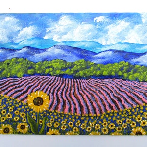 May include: A painting of a field of sunflowers in the foreground with a field of lavender in the middle ground and a mountain range in the background. The sky is blue with white clouds.