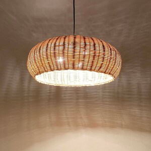 May include: A round, woven wicker pendant light fixture in a natural brown colour. The light is switched on and illuminates the room.