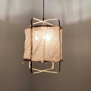 May include: A brown fabric lampshade with a wooden frame hangs from the ceiling. The lampshade is lit and casts a warm glow.