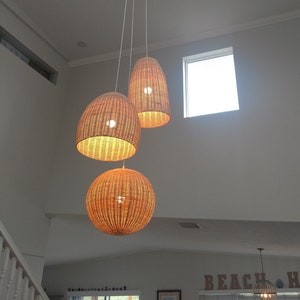 May include: Three woven wicker pendant lights hang from the ceiling in a room with white walls and a window. The lights are round and have a natural brown color.