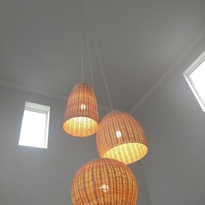 May include: Three woven wicker pendant lights hanging from the ceiling. The lights are round and oval shaped and have a natural brown color.