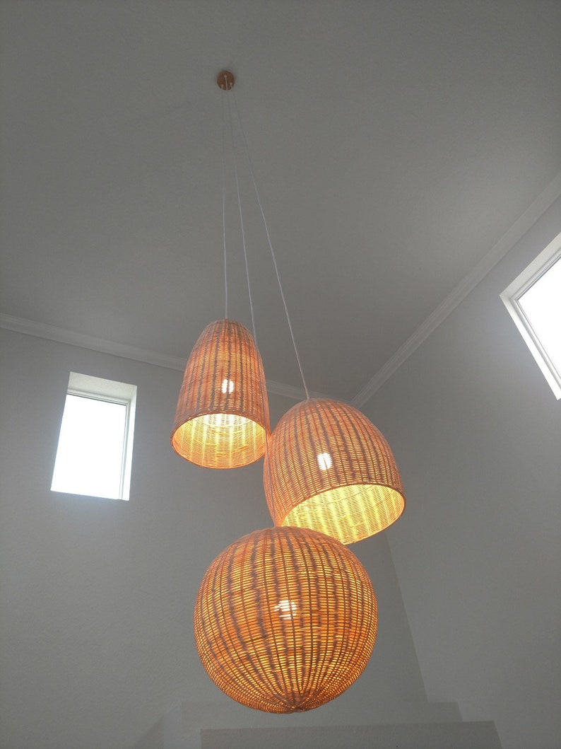 May include: Three woven wicker pendant lights hanging from the ceiling. The lights are round and oval shaped and have a natural brown color.