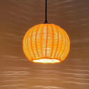 May include: A round, woven pendant light fixture with a natural, light brown color. The light is turned on and illuminates the room.