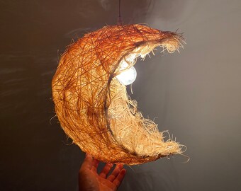 May include: A crescent moon-shaped pendant light made of natural fibers, with a white light bulb illuminating the interior.