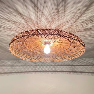 May include: A circular rattan pendant light fitting. The light fitting is brown and has a light bulb in the centre. The light casts a shadow on the ceiling.