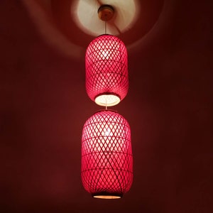 Puede incluir: Dos lámparas colgantes de mimbre rojo cuelgan del techo. Las luces están encendidas y emiten un brillo cálido.