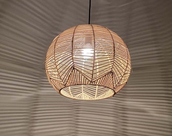 May include: A woven rattan pendant light fixture with a geometric pattern. The light is turned on and illuminates the room.