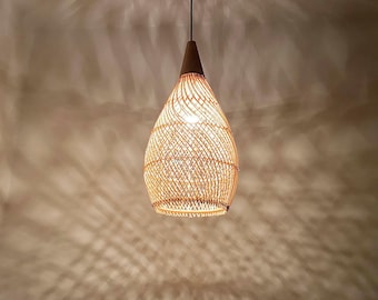 Könnte beinhalten: Hängeleuchte in Tropfenform mit geflochtenem Rattanschatten und dunkelbraunem Holzaufsatz. Die Leuchte hängt an einem schwarzen Kabel und strahlt ein warmes Licht aus. Der Schirm besteht aus dünnen, hellbraunen Rattanstreifen.