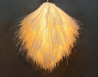 May include: A white, fluffy, round pendant light fixture made of thin, stringy material. The light is on and emits a warm, yellow glow.