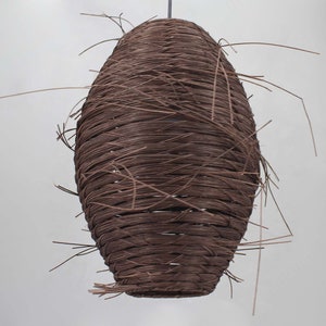May include: A brown woven pendant light fixture with a natural, organic texture. The light fixture is made of thin, interwoven strands of material, creating a unique and rustic look.