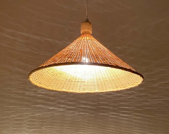 May include: A woven wicker pendant light fixture with a conical shade. The light is turned on and illuminates the room.