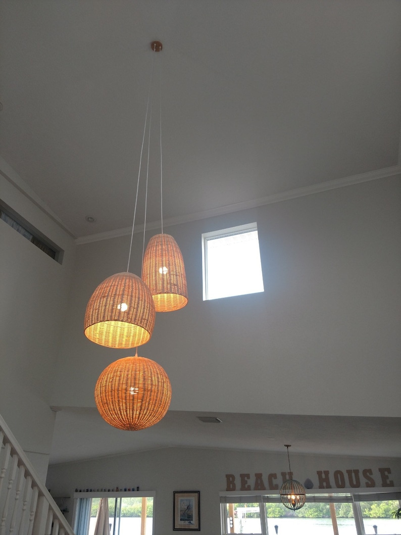 May include: Three woven wicker pendant lights hang from the ceiling in a room with white walls and a window. The lights are round and have a natural brown color.