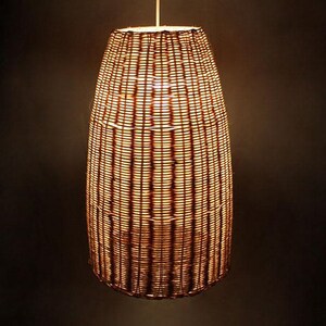 May include: A woven wicker pendant light fixture with a warm, golden glow. The light is shaped like a tall, narrow cylinder.