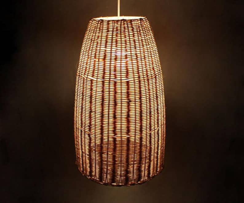 May include: A woven wicker pendant light fixture with a warm, golden glow. The light is shaped like a tall, narrow cylinder.