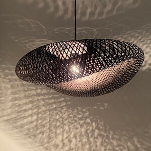 Può includere: Un lampadario a sospensione in vimini nero con un design moderno e unico. Il lampadario è realizzato con sottili strisce di materiale intrecciate, creando un motivo geometrico.