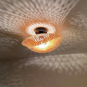 May include: A woven bamboo ceiling light fixture with a round, open design. The light casts a patterned shadow on the ceiling.