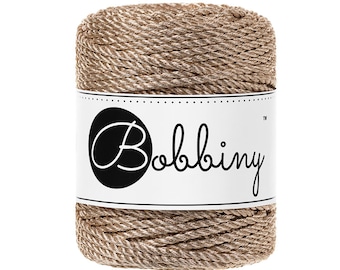 May include: A spool of gold and brown metallic yarn with the word "Bobbiny" printed on the label.