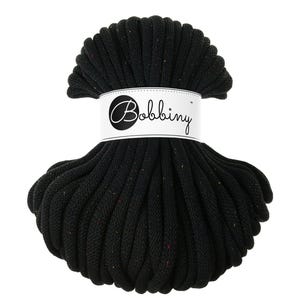 Puede incluir: Un ovillo de cordón de macramé negro con motas de color, envuelto con una etiqueta blanca que dice "Bobbing". El cordón, bien enrollado, es adecuado para proyectos de manualidades, como tapices de macramé o colgadores de plantas.