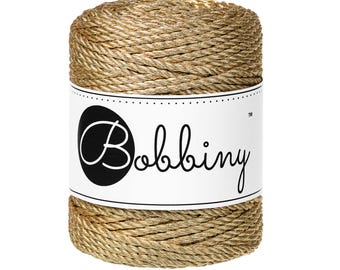 May include: A spool of gold metallic rope yarn with a white label that says "Bobbiny™".