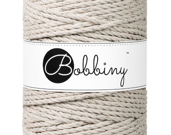 May include: A spool of natural colored cotton rope with a white label that says "Bobbiny" in black script.