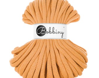 May include: A close-up of a large spool of thick, orange cotton rope. The rope is tightly wound and has a label that reads "Bobbiny".