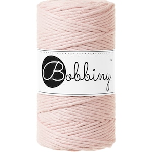 Puede incluir: Un rollo de cuerda de algodón rosa pálido con una etiqueta blanca que dice "Bobbiny™".