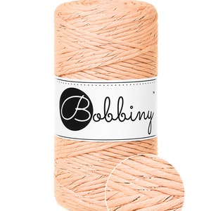 May include: A spool of peach colored yarn with gold metallic thread running through it. The yarn is labeled "Bobbiny".