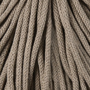 May include: Close-up of a bundle of thick, braided rope in a neutral beige color. The rope has a textured surface with visible woven patterns. The strands are tightly packed together, creating a dense and durable appearance. The rope is suitable for various crafting and decorative projects.