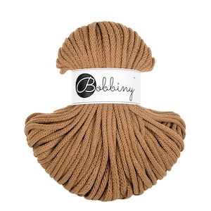 May include: A close-up of a brown cotton cord, wound into a ball shape. The cord is labelled with a white tag that reads "Bobbiny".