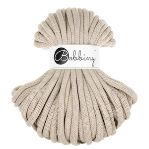 Puede incluir: Un cordón de algodón beige, enrollado en un círculo, con una etiqueta blanca que dice "Bobbiny" en letras negras.