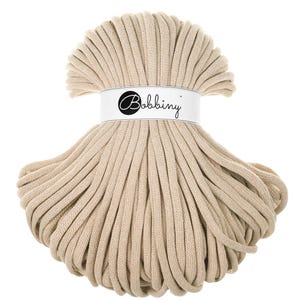 Può includere: Un cordoncino di cotone beige, avvolto a cerchio, con un'etichetta bianca su cui è scritto "Bobbiny".