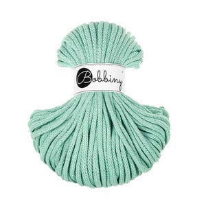 May include: A bundle of mint green macrame cord. The cord is wrapped with a white label that reads "Bobbing" in a script font. The cord is tightly wound and has a textured appearance, suitable for various crafting projects.