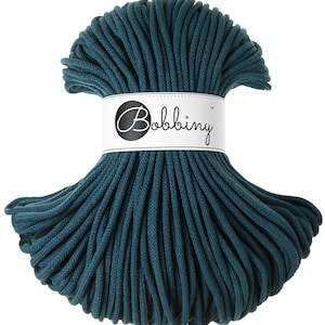 May include: Teal cotton cord, a thick, twisted rope, is wound into a circle. The cord is labeled "Bobbiny" on a white tag.